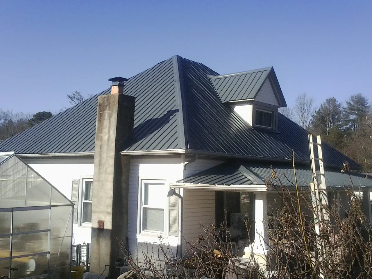 Dark blue standing seam metal roof on a white farmhouse with dormer — Slate & Tile Roof Repair by Roofing Brothers in Park City
