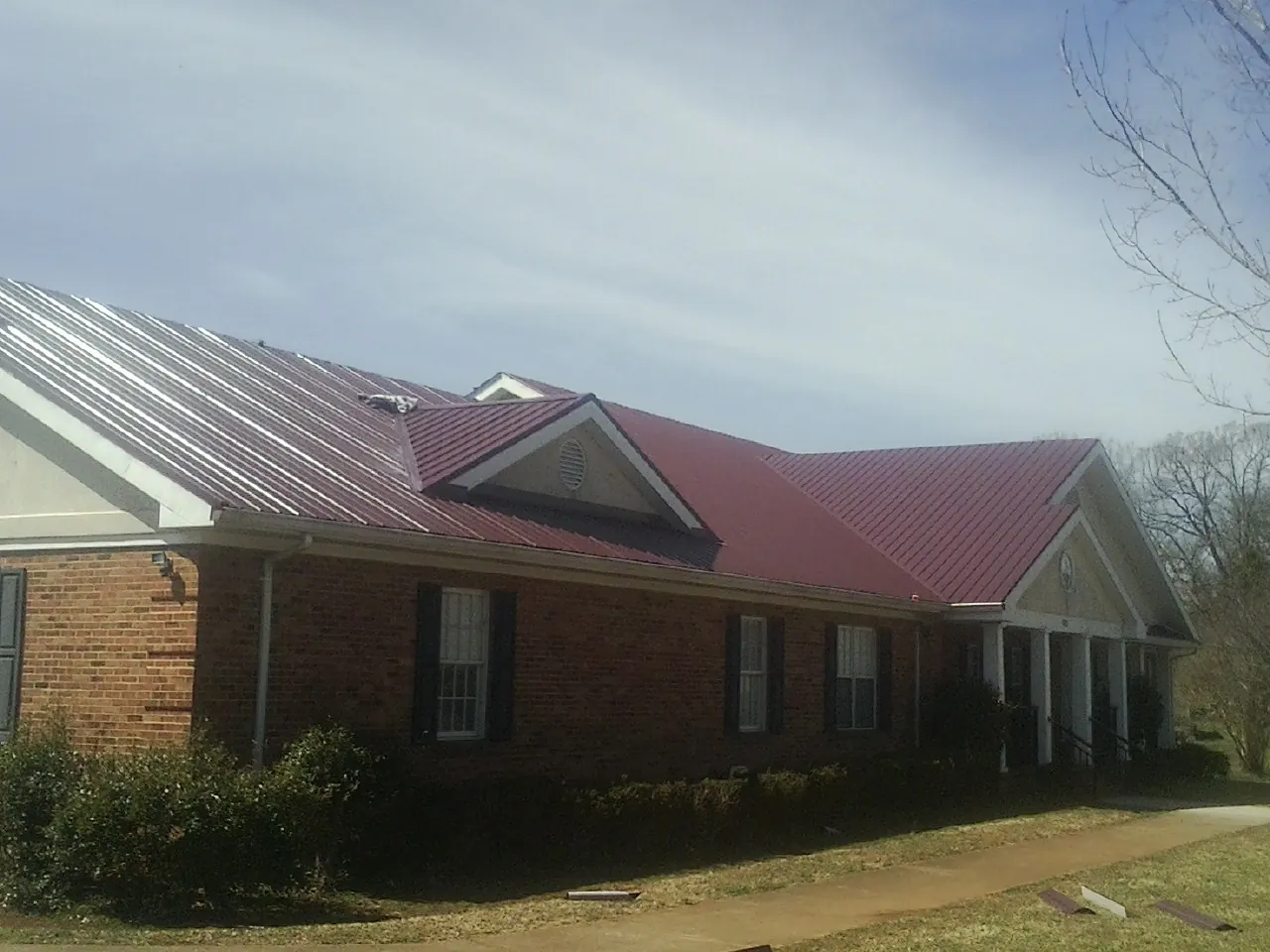 Red metal roof with gabled entries on a long brick building, from a Hail Damage Roof Repair job in Park City