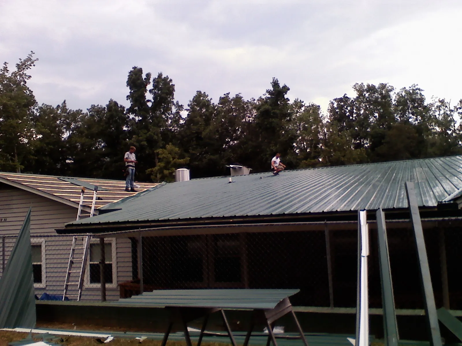 Two roofers installing green metal panels above a covered porch in Park City